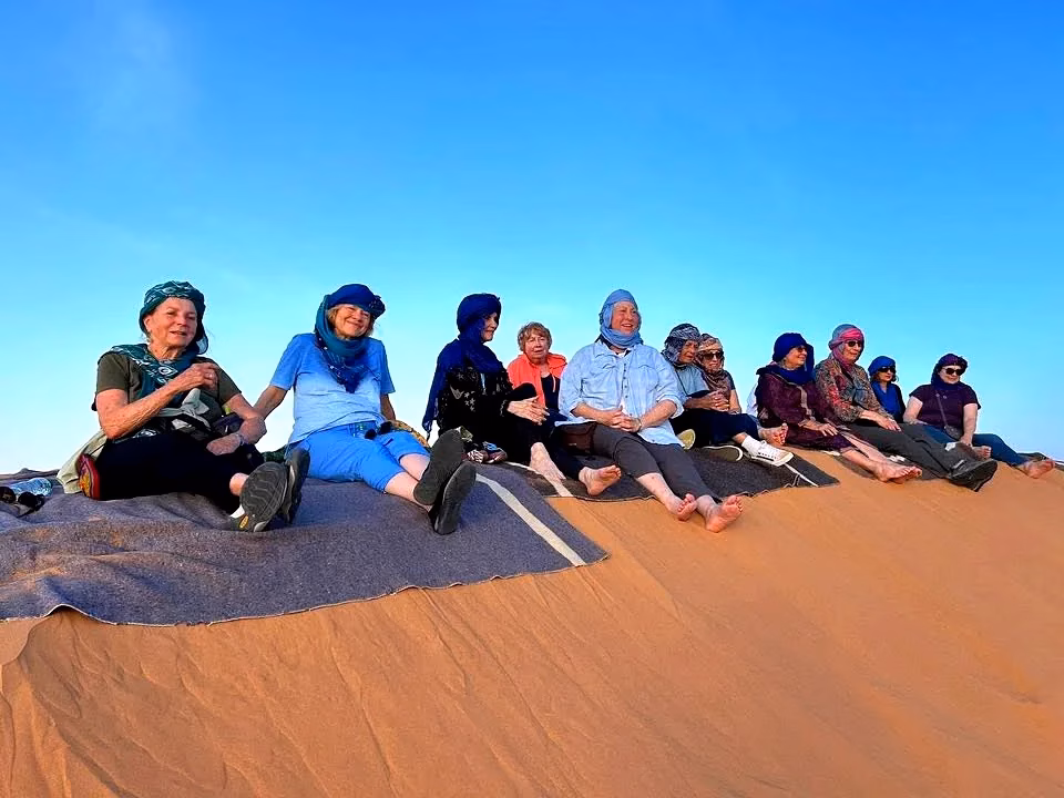 Tour da Errachidia a Merzouga - Gruppo di turisti seduti sulle dune Erg Chebbi al tramonto con turbanti blu - Tour privato da aeroporto ERH ZagoraExperience